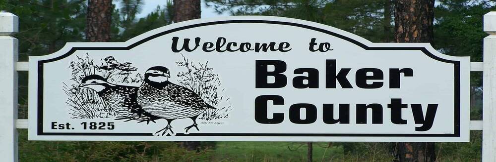 A white sign with birds drawn on it. The sign says Welcome to Baker County.